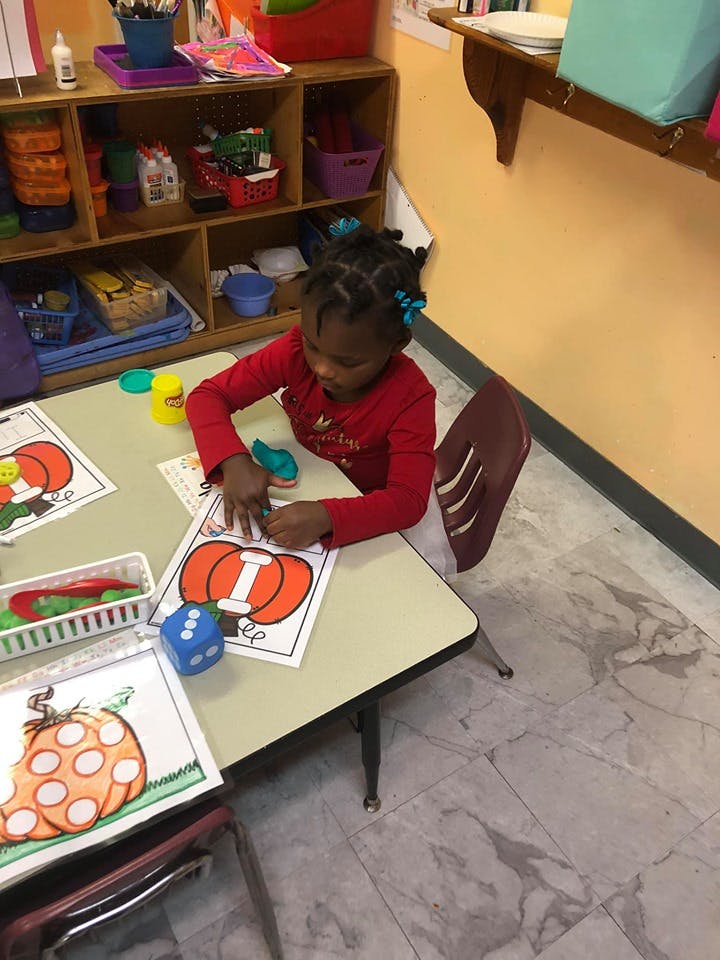 Child at a table working on a craft with a pumpkin outline
