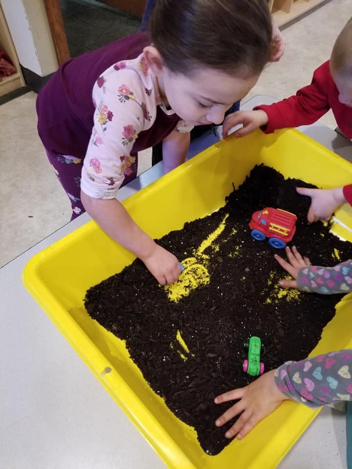 Child playing with dirt and toys in a yellow bin