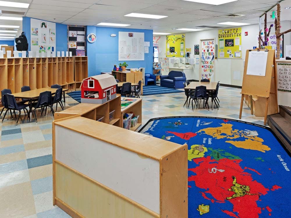 Classroom with tables and chairs, cubbies, a map rug, and a toy barn