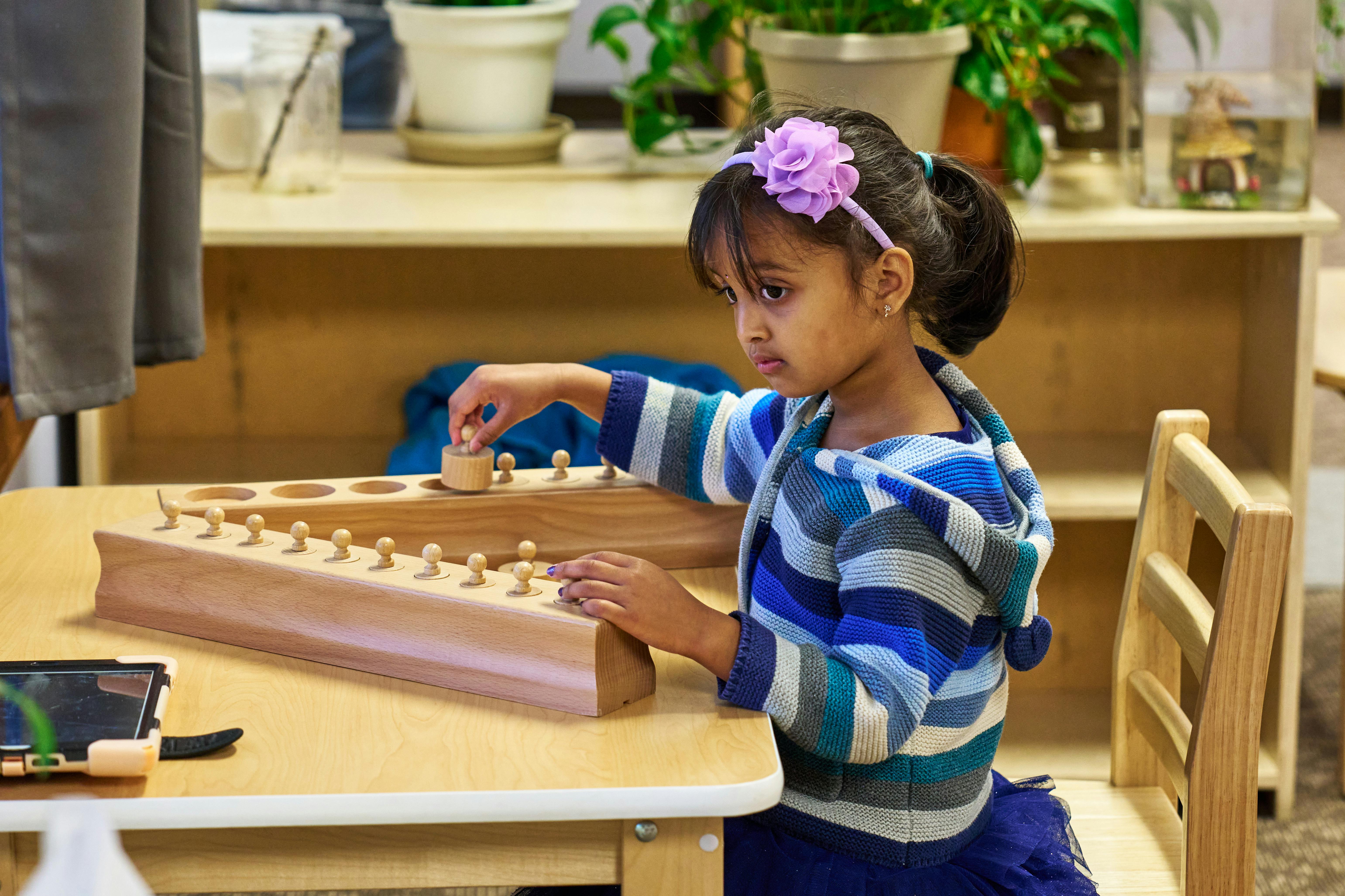 Child playing with a wooden peg and hole toy at a table