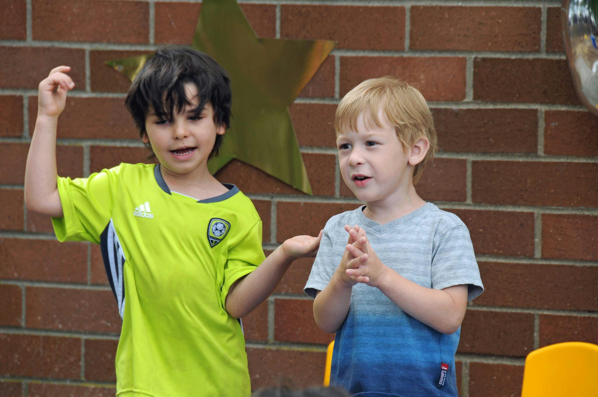 Two children standing, one gesturing and one clapping
