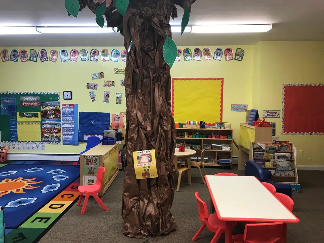 Classroom with a tree decoration, small tables and chairs, and colorful rugs