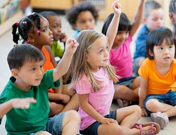 Children sitting on the floor with some raising their hands