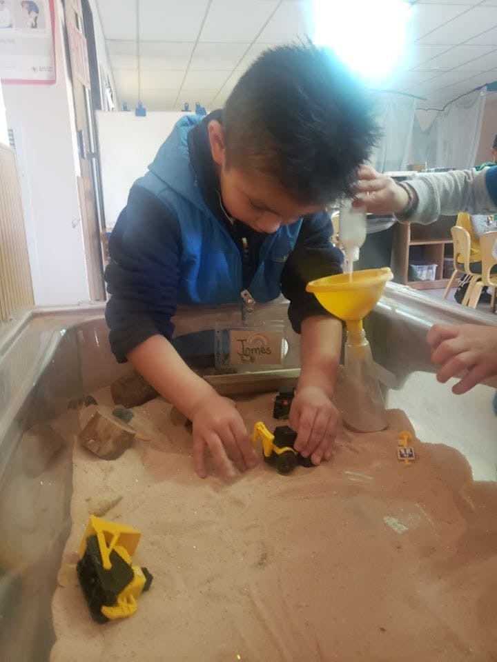 Child playing with sand and toy construction vehicles