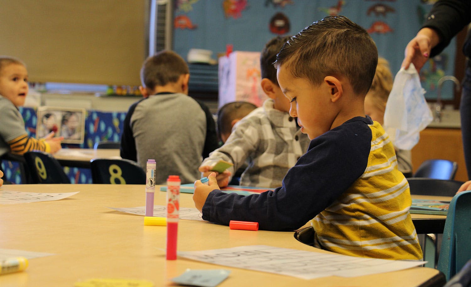 Child drawing at a table with other children in a classroom