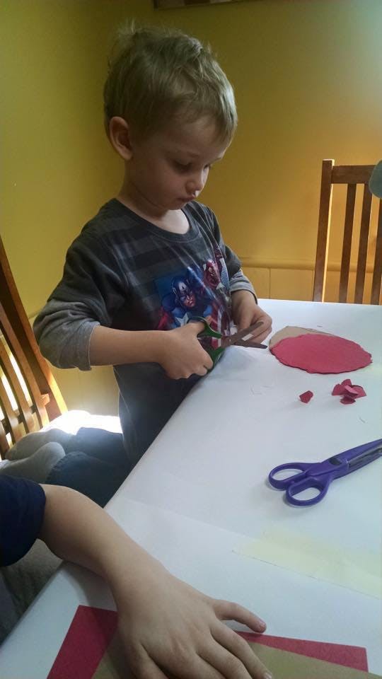 Child cutting red paper with scissors at a table