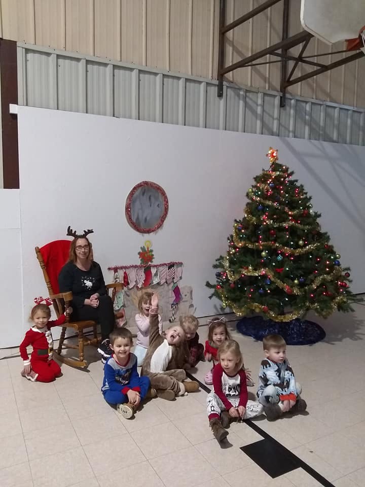 Person in reindeer antlers sitting in a rocking chair with children onlooking children