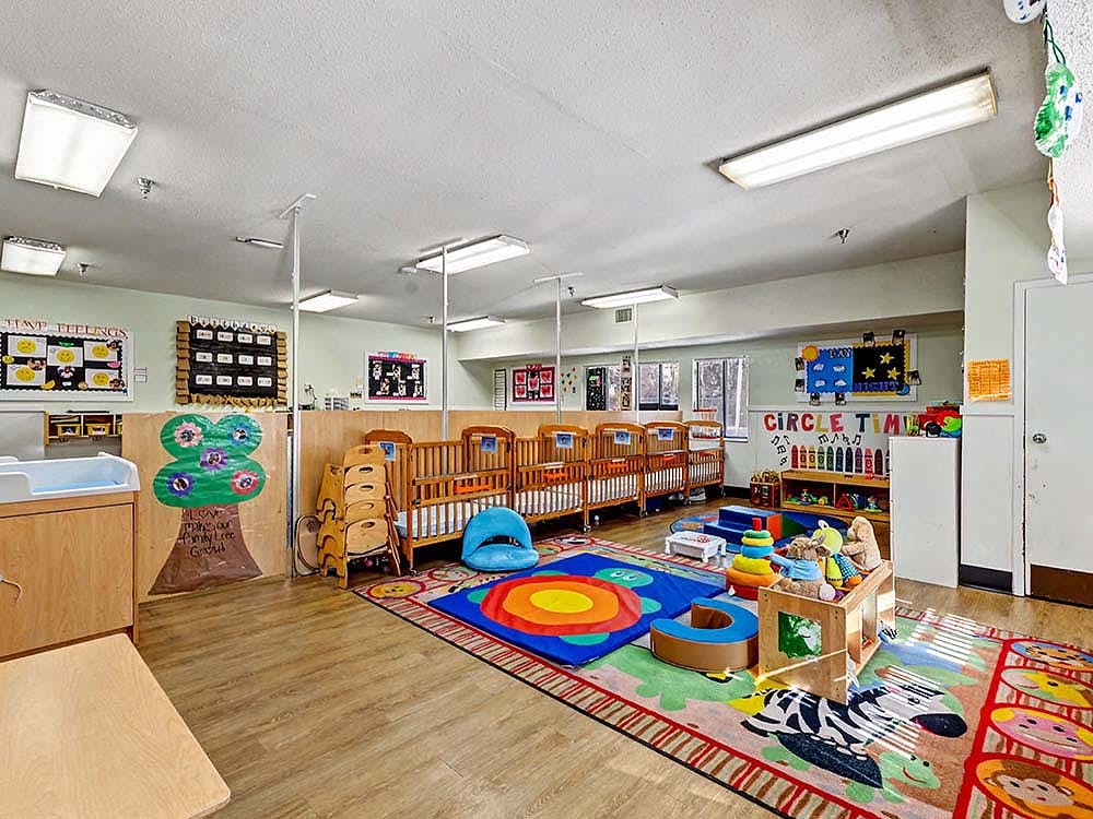 A colorful childcare room with cribs, play mats, and learning charts