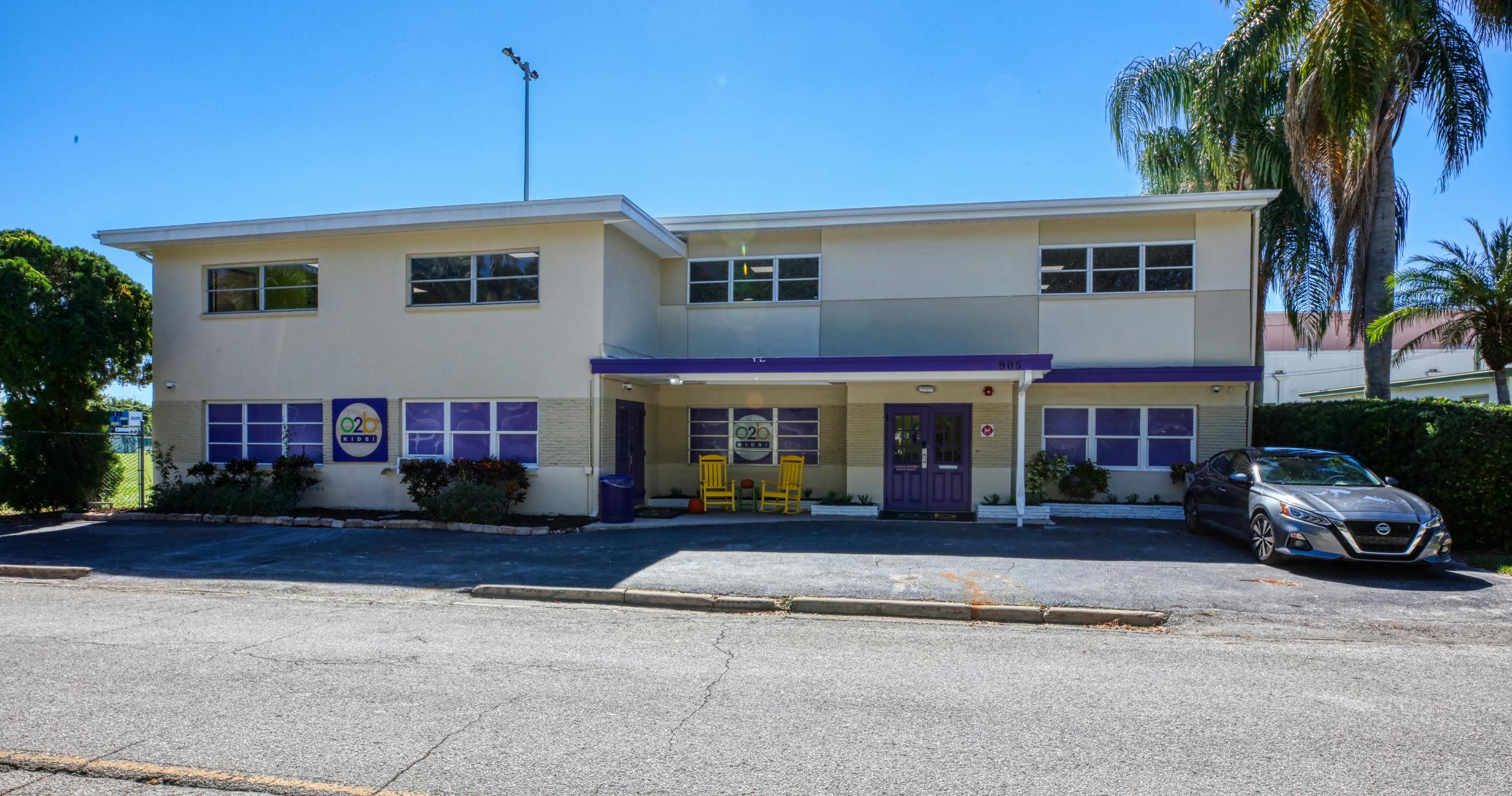 A beige two-story building with purple accents and a parked car