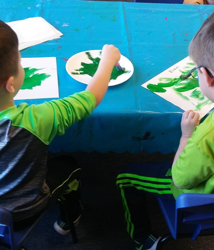 Two children painting with green paint at a table