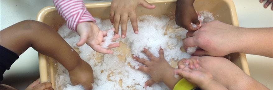 Multiple children's hands playing in a bin of white fluffy material