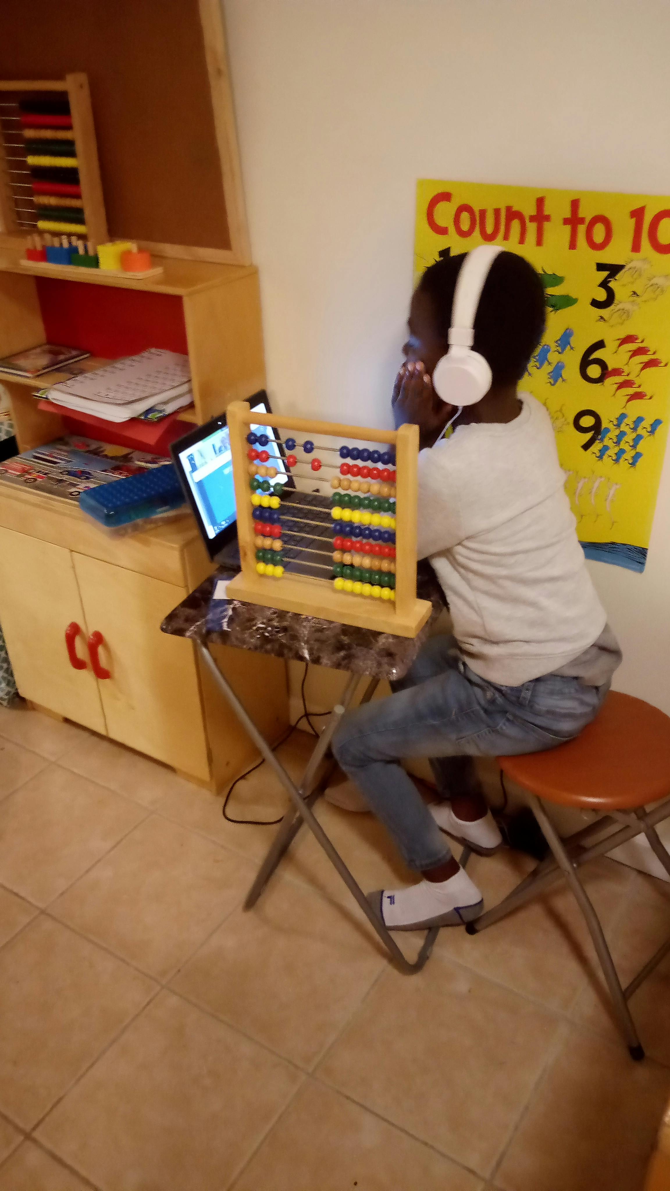 Child wearing headphones looking at a tablet with an abacus on a table
