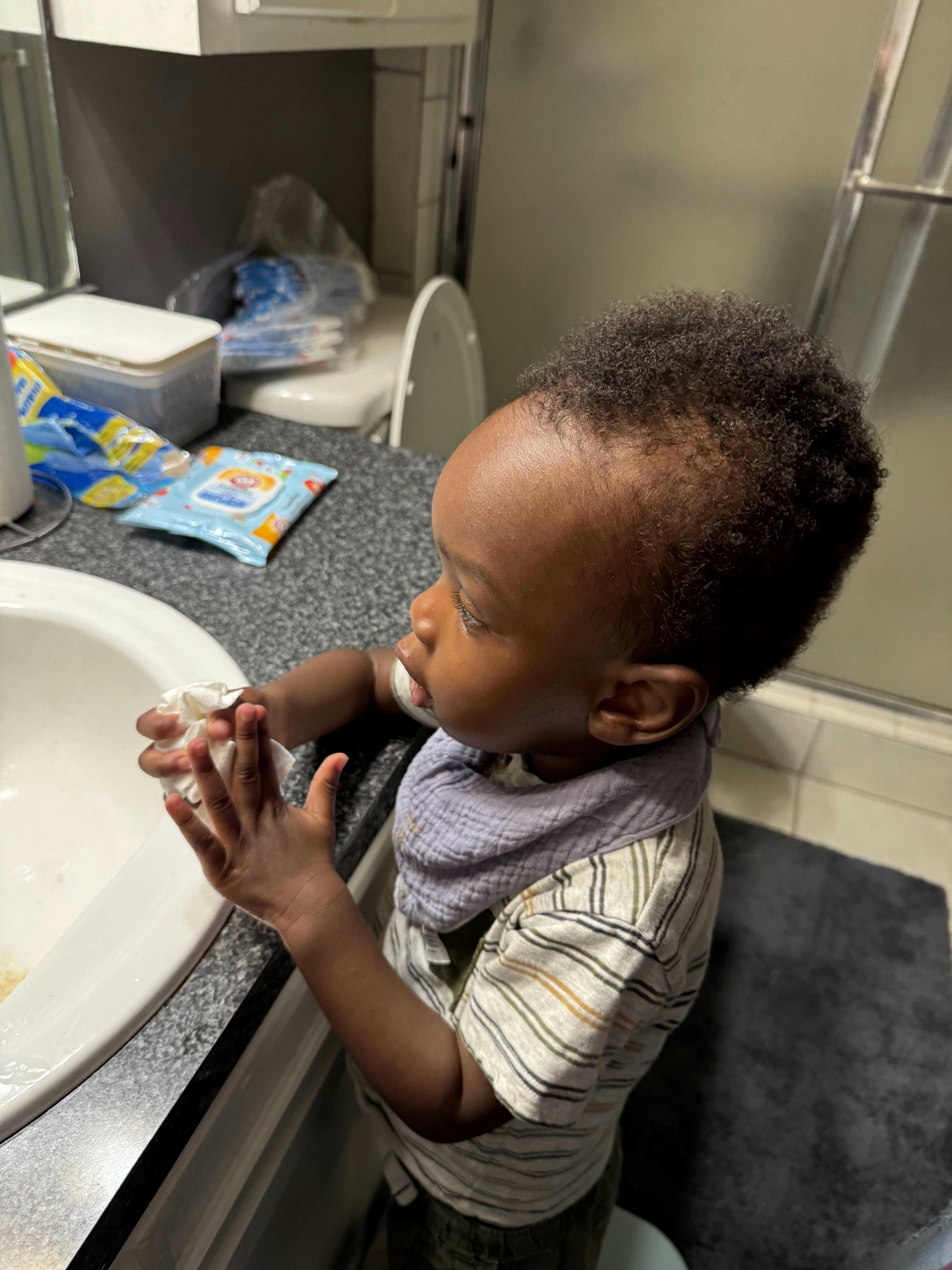 Child standing at a sink, holding a white cloth