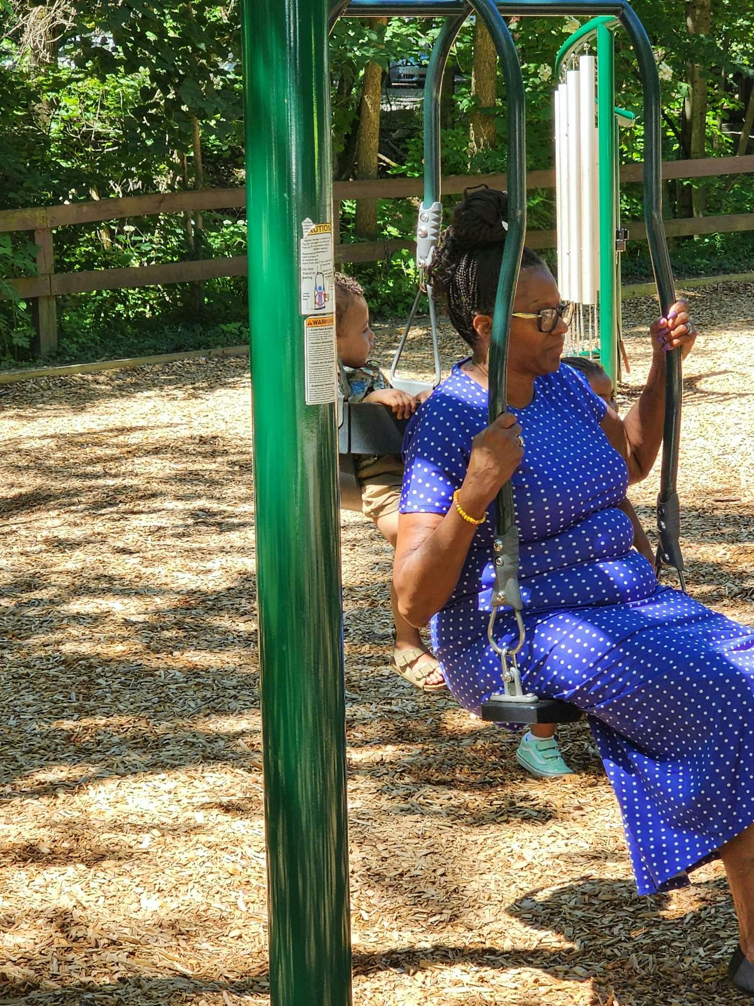 Person in a blue dress swinging on a playground, child in a swing behind them