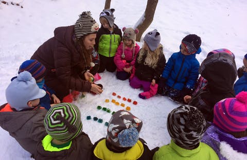 Adult and children sitting in a circle in the snow with colorful objects