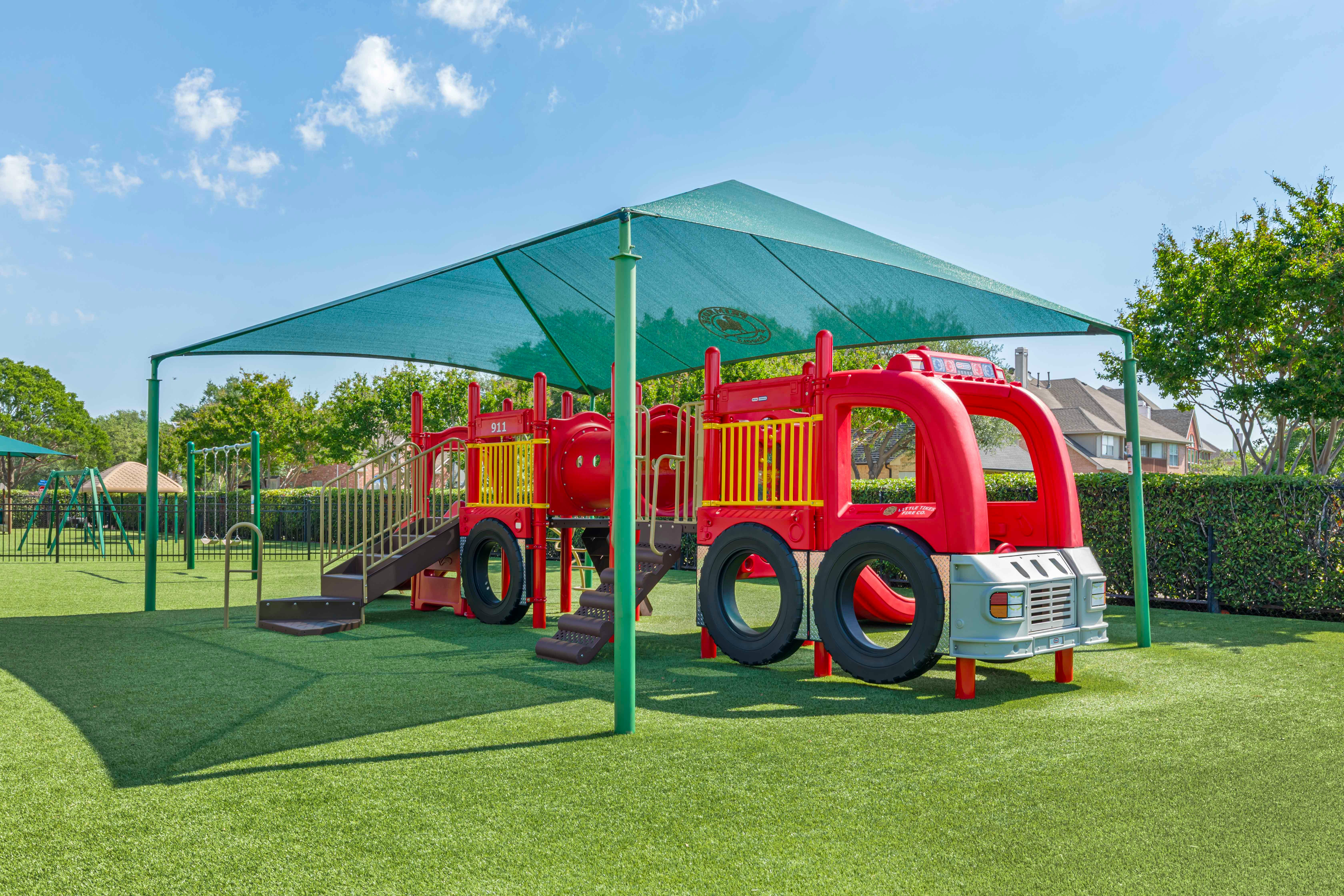 Red fire truck-shaped play structure on green artificial turf