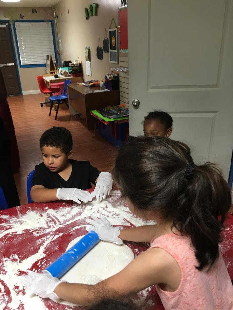 Child rolling dough with a rolling pin, another child watching
