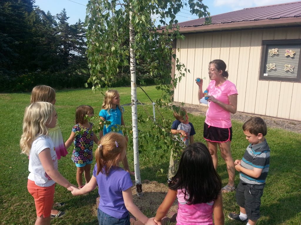 Adult and children gathered around a small tree, some holding hands