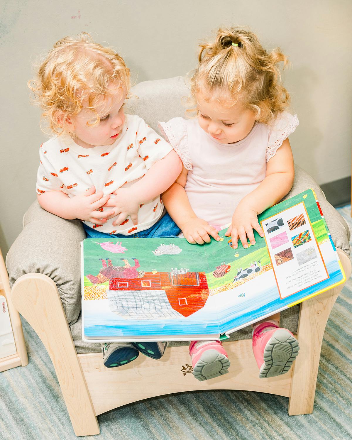 Two children sitting together on a chair, looking at an open book