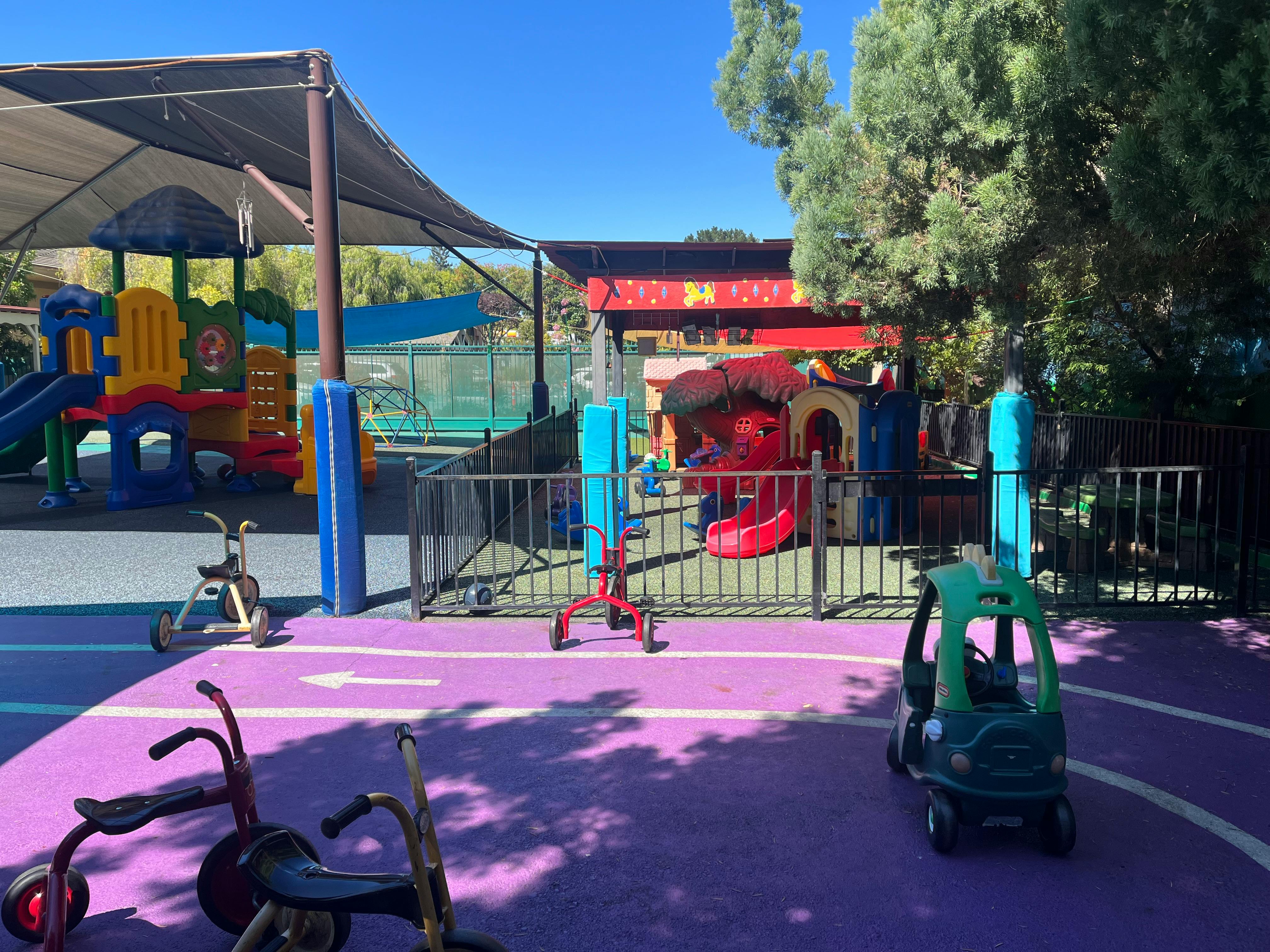 Outdoor playground with colorful play structures and tricycles on purple ground