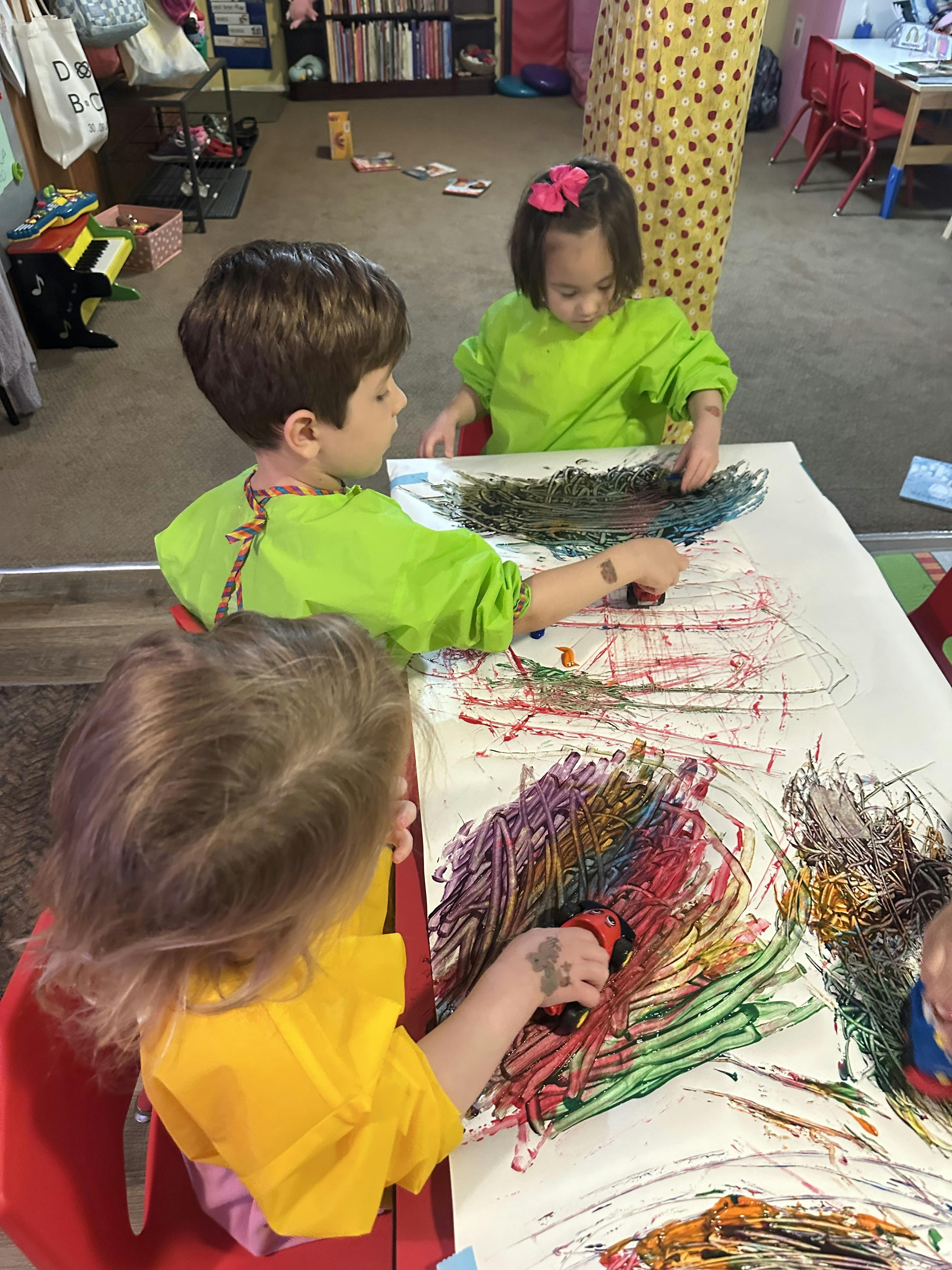 Three children in art smocks finger painting with bright colors