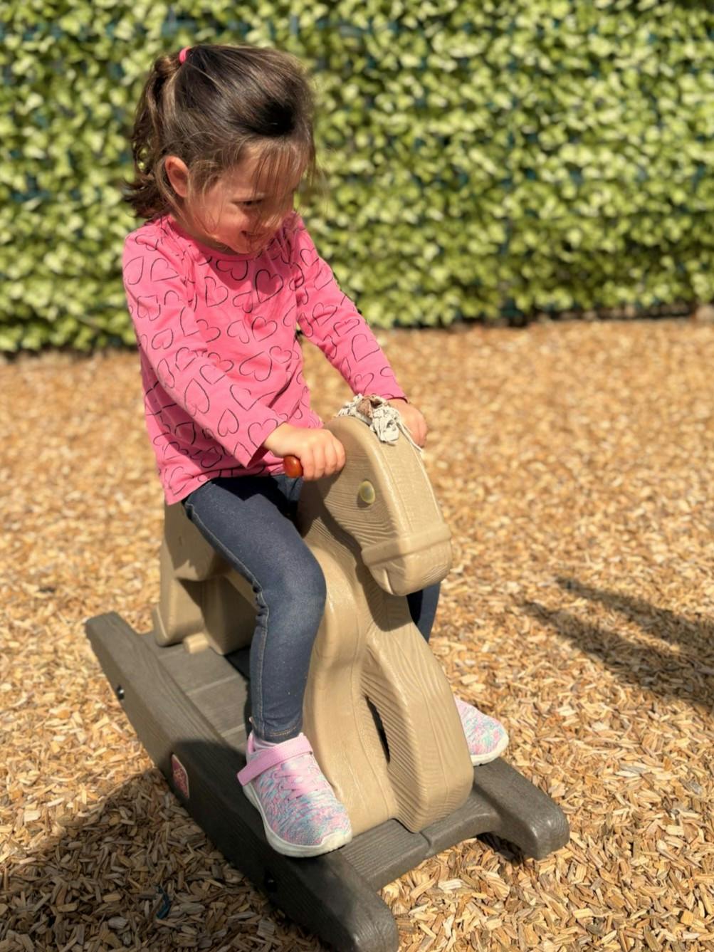 Child riding a plastic rocking horse on a wood chip playground surface