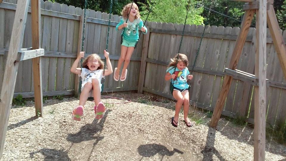 Three children on swings in a backyard