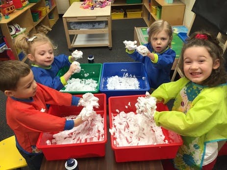 Four children playing with shaving cream in red, green, and blue bins