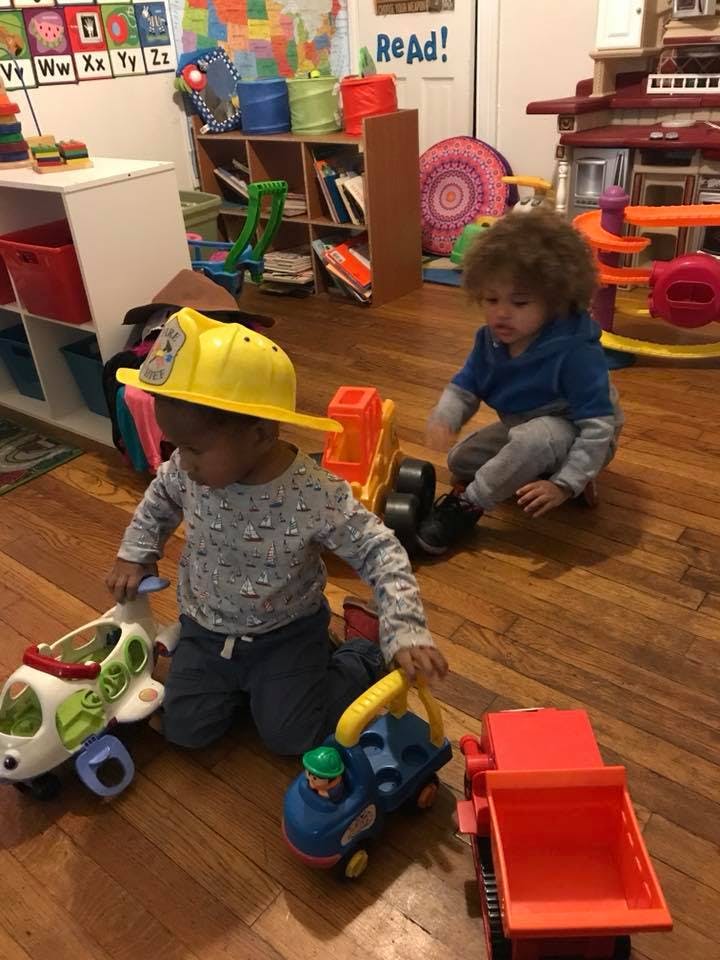 Two children playing with toy vehicles on a wooden floor