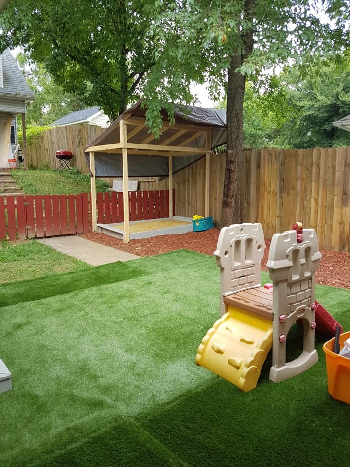 Backyard with artificial turf, a sandbox under a canopy, and a small slide