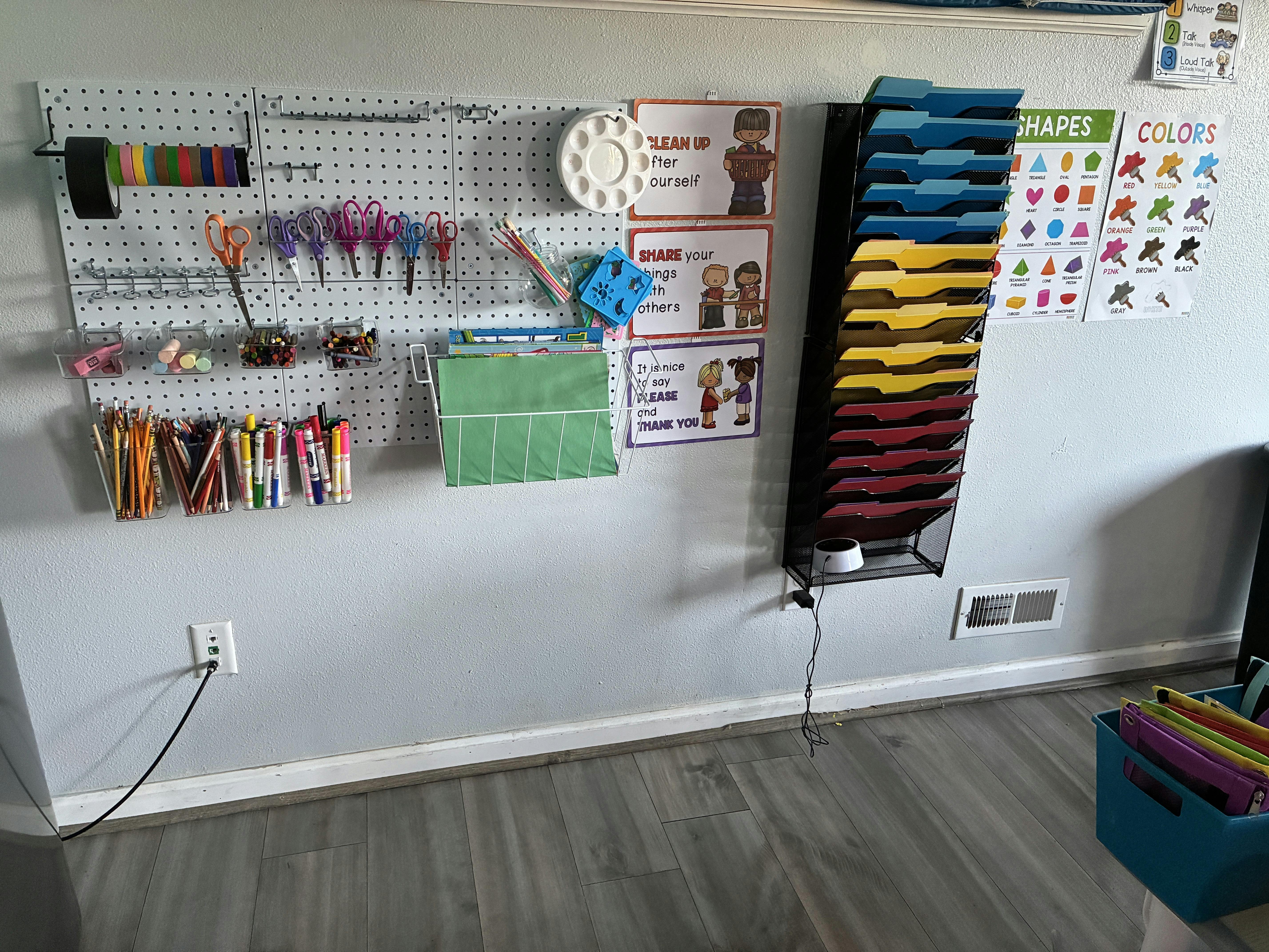 Pegboard with art supplies and organizers, posters of shapes, colors, and classroom rules