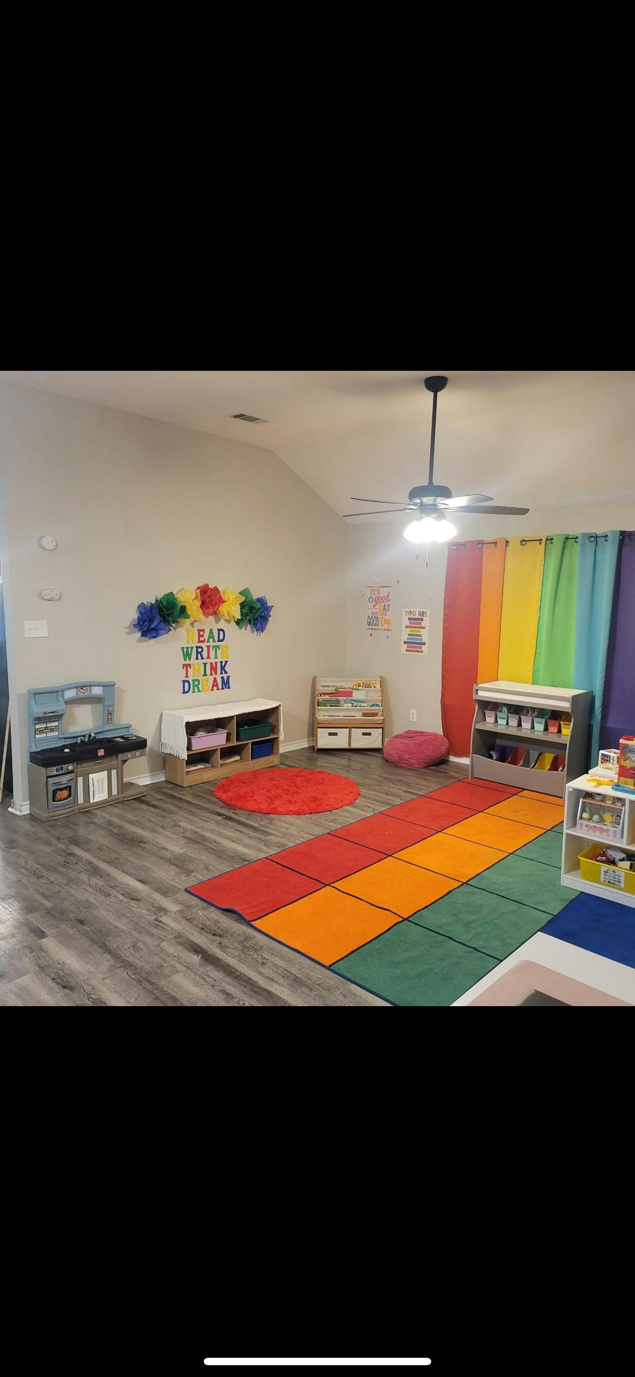 Playroom with colorful rugs, toy kitchen, and shelves with "Read Write Think Dream" on wall