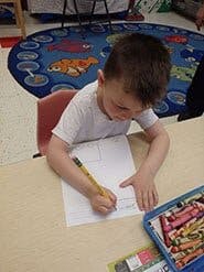 Child drawing on paper with a pencil at a table
