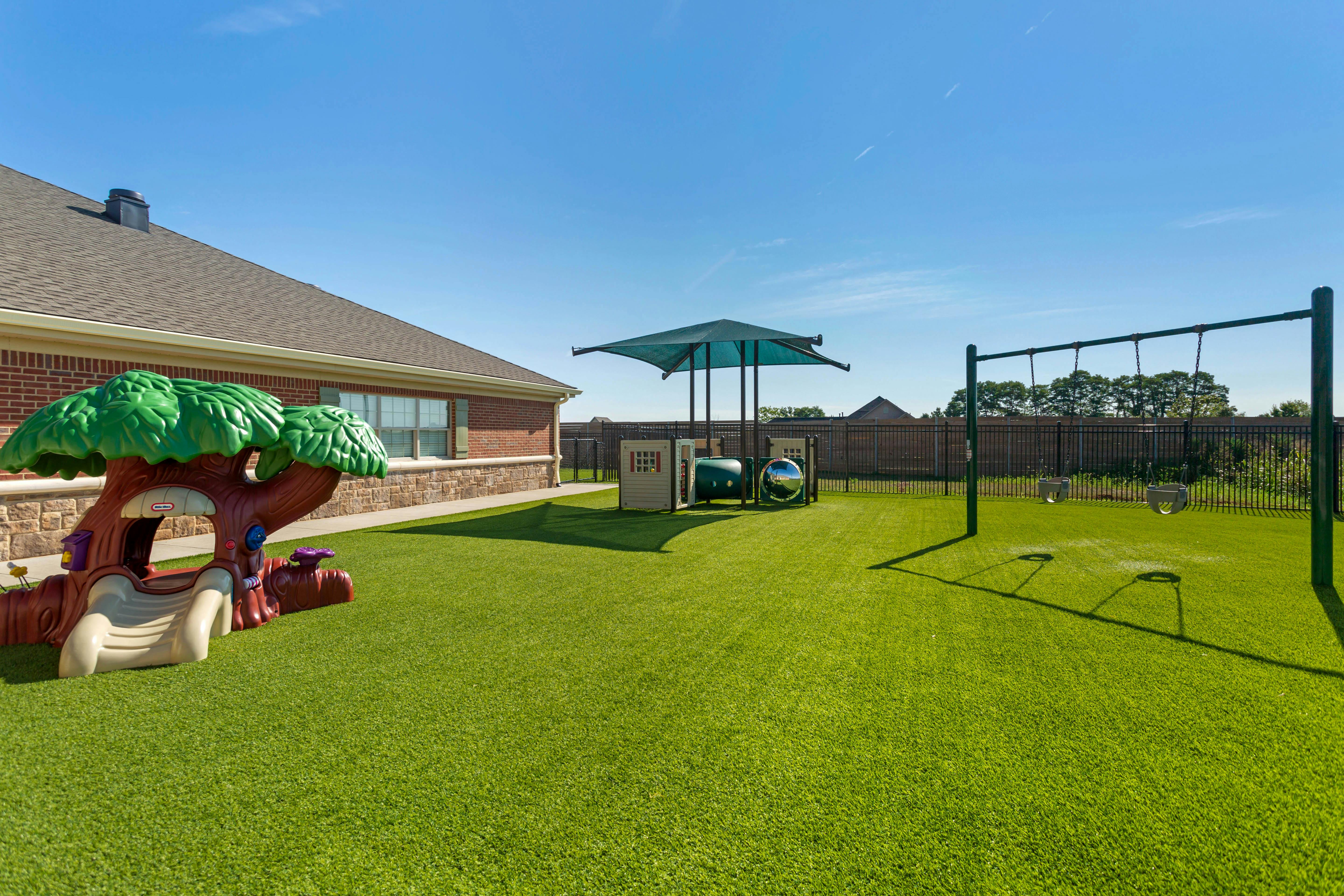 Outdoor playground area with a play structure, swings, and shade structure