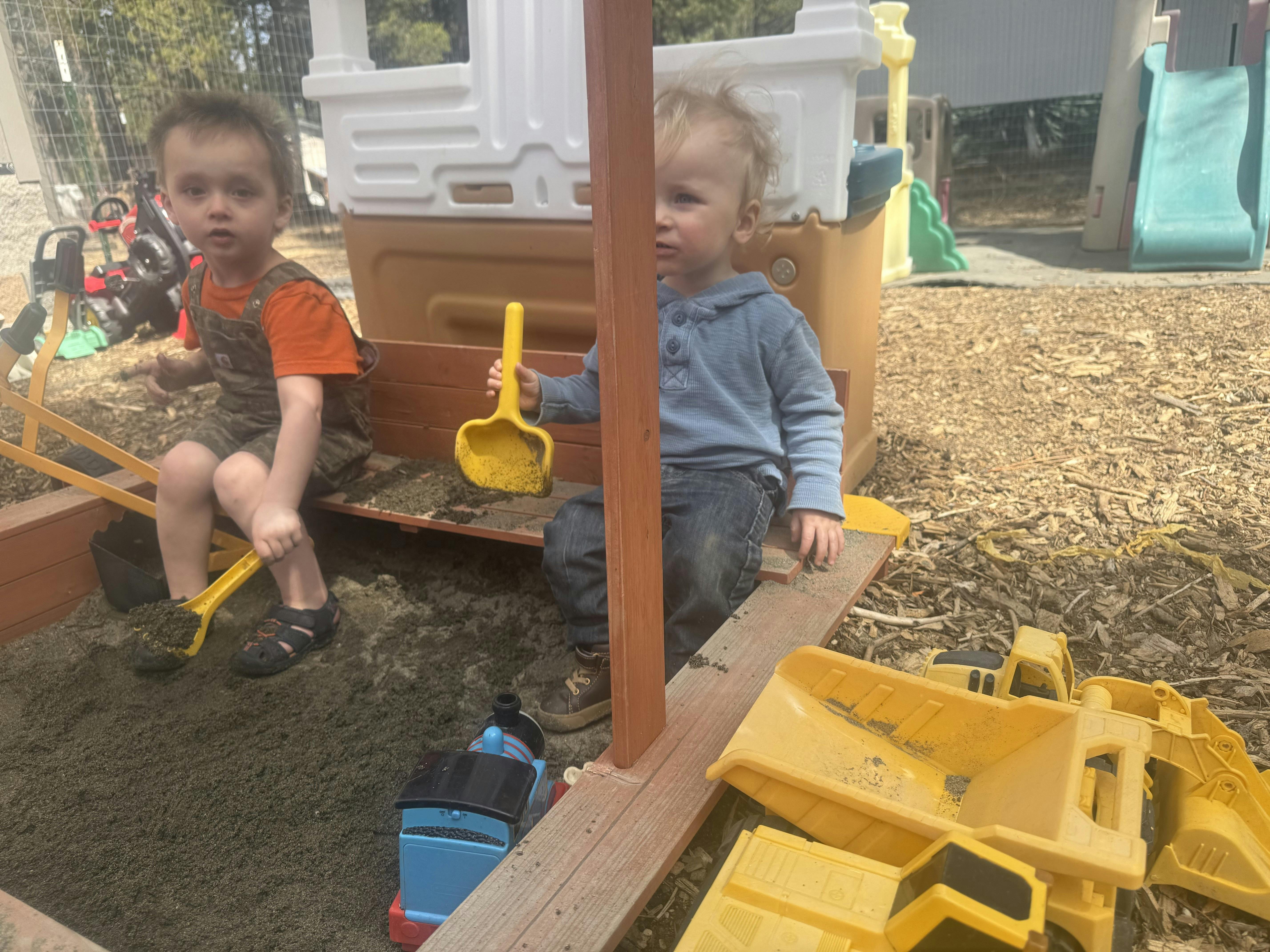 Two children playing in a sandbox with shovels