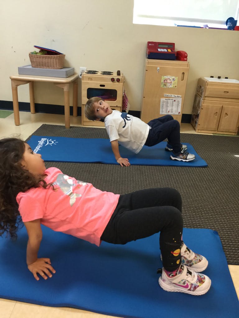 Two children doing crab walks on blue mats in a classroom