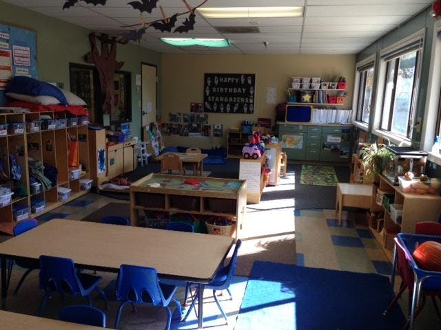 A classroom with tables, chairs, storage cubbies, and windows