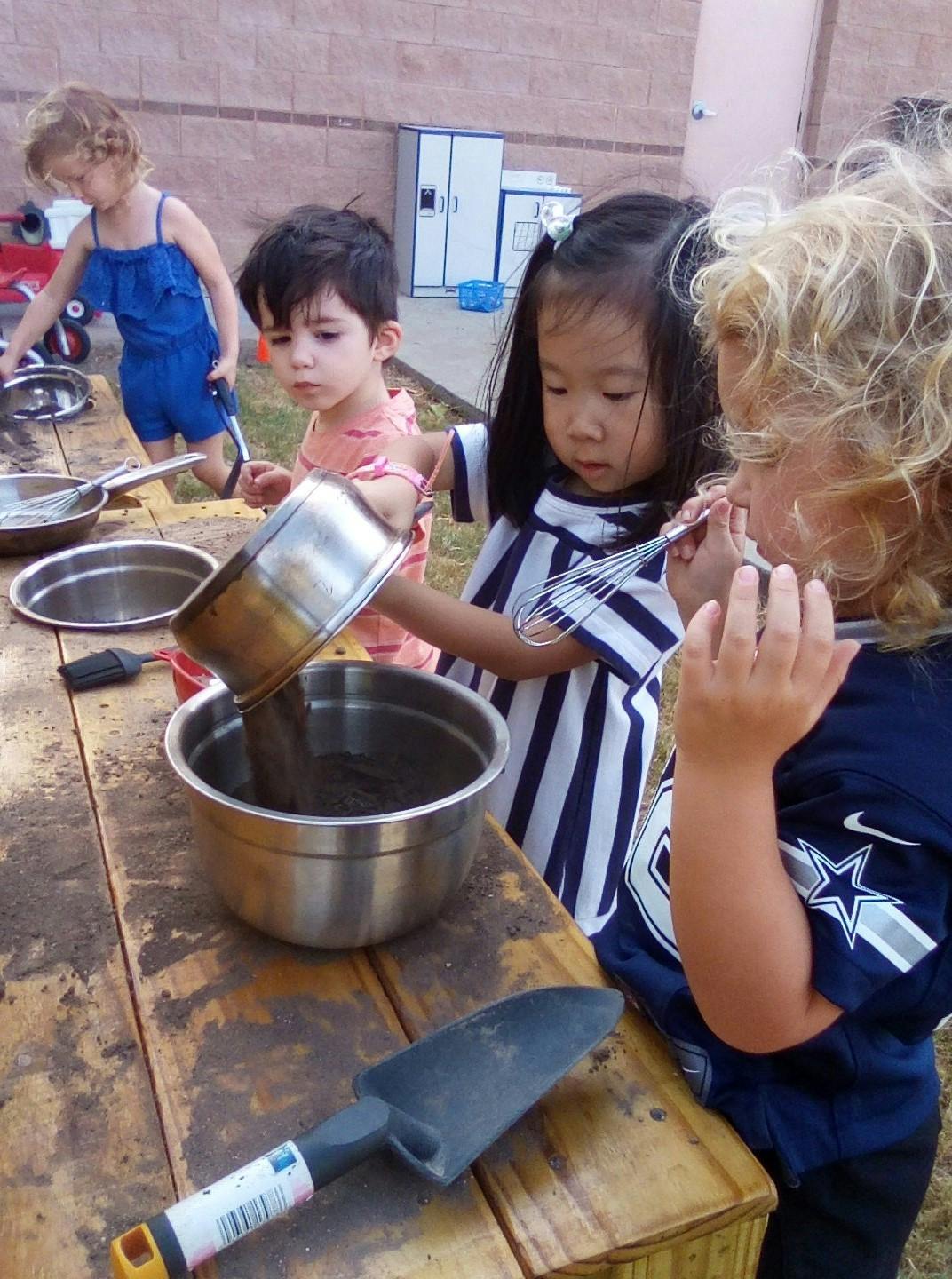 Children playing with water and bowls at a wooden table