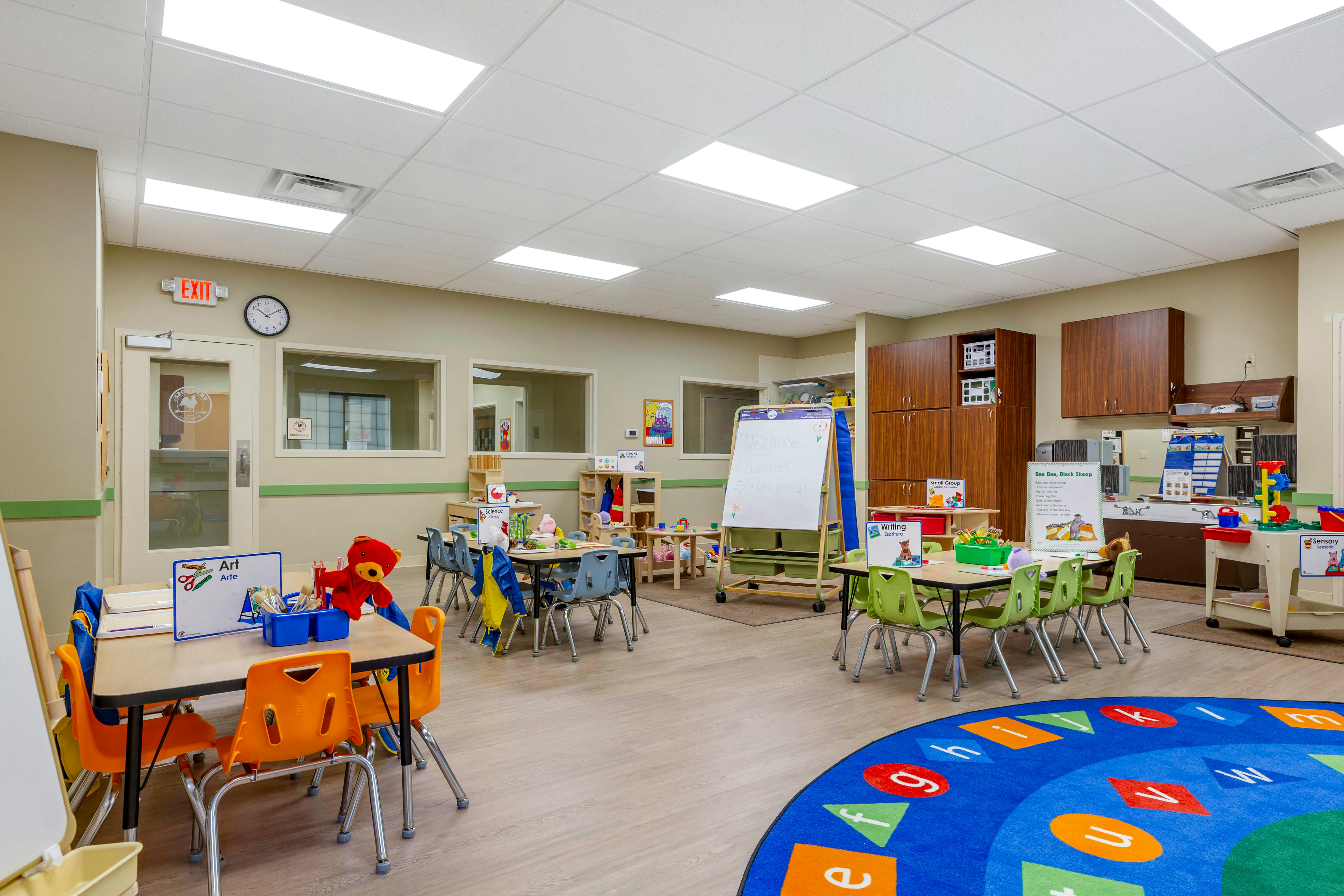 An empty preschool classroom with small tables and chairs, toys, and educational posters