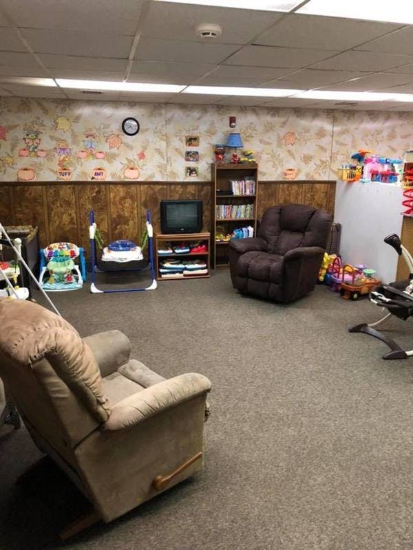 Room with two recliners, baby swings, television, and bookshelf