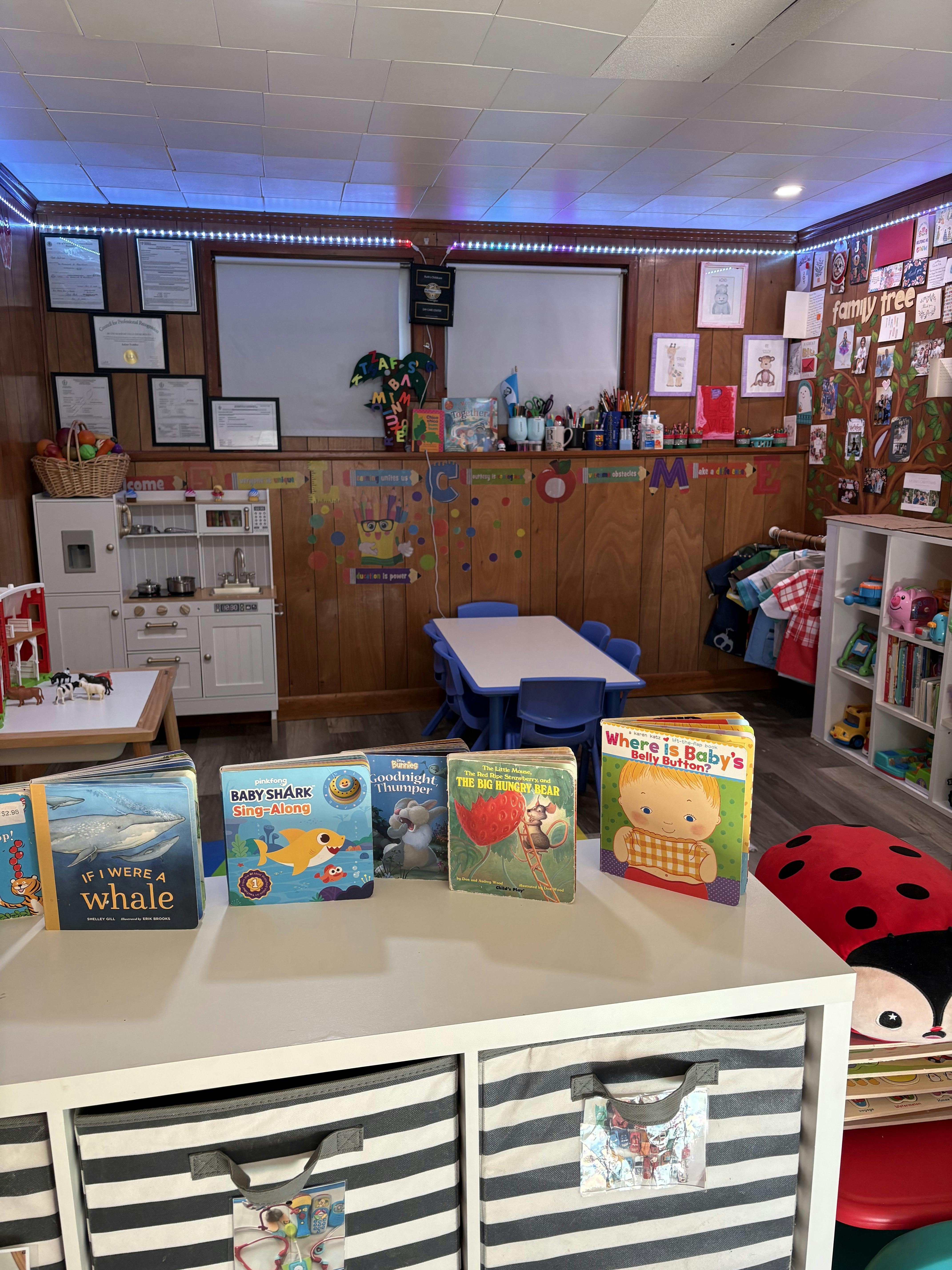 Children's books displayed on a white shelf in a classroom with a play kitchen