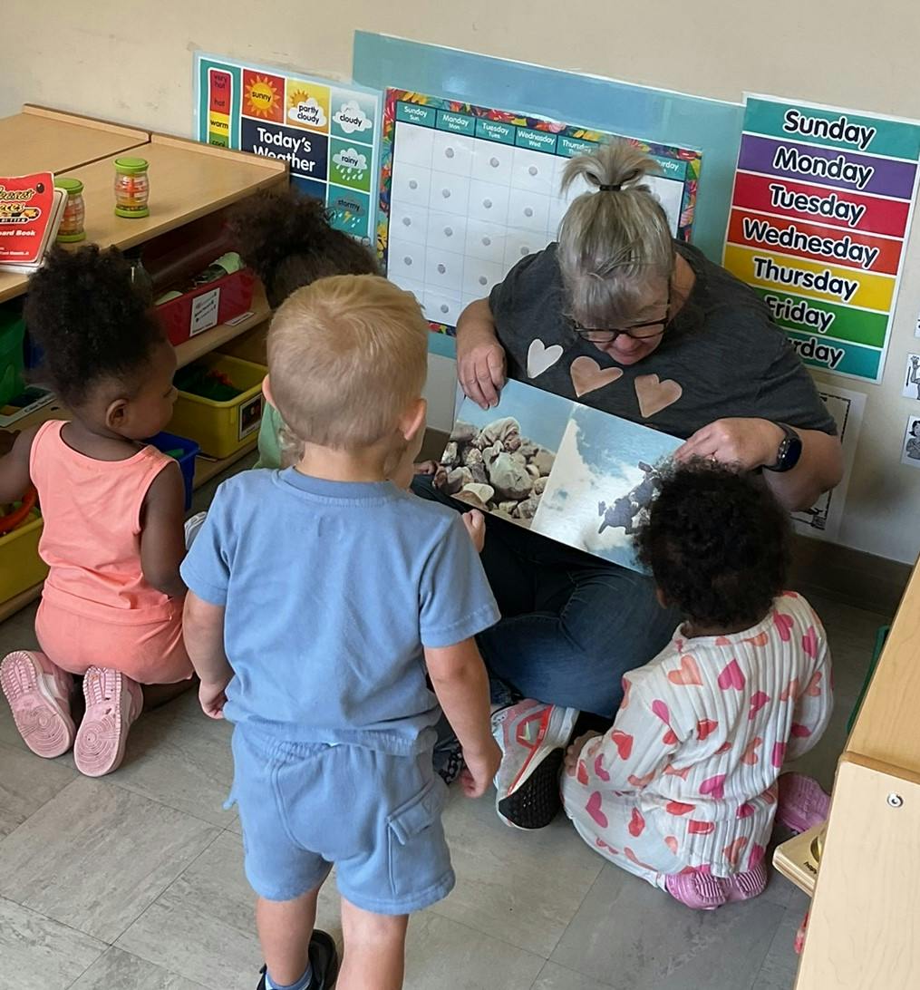 Adult reading a book to three children in a classroom