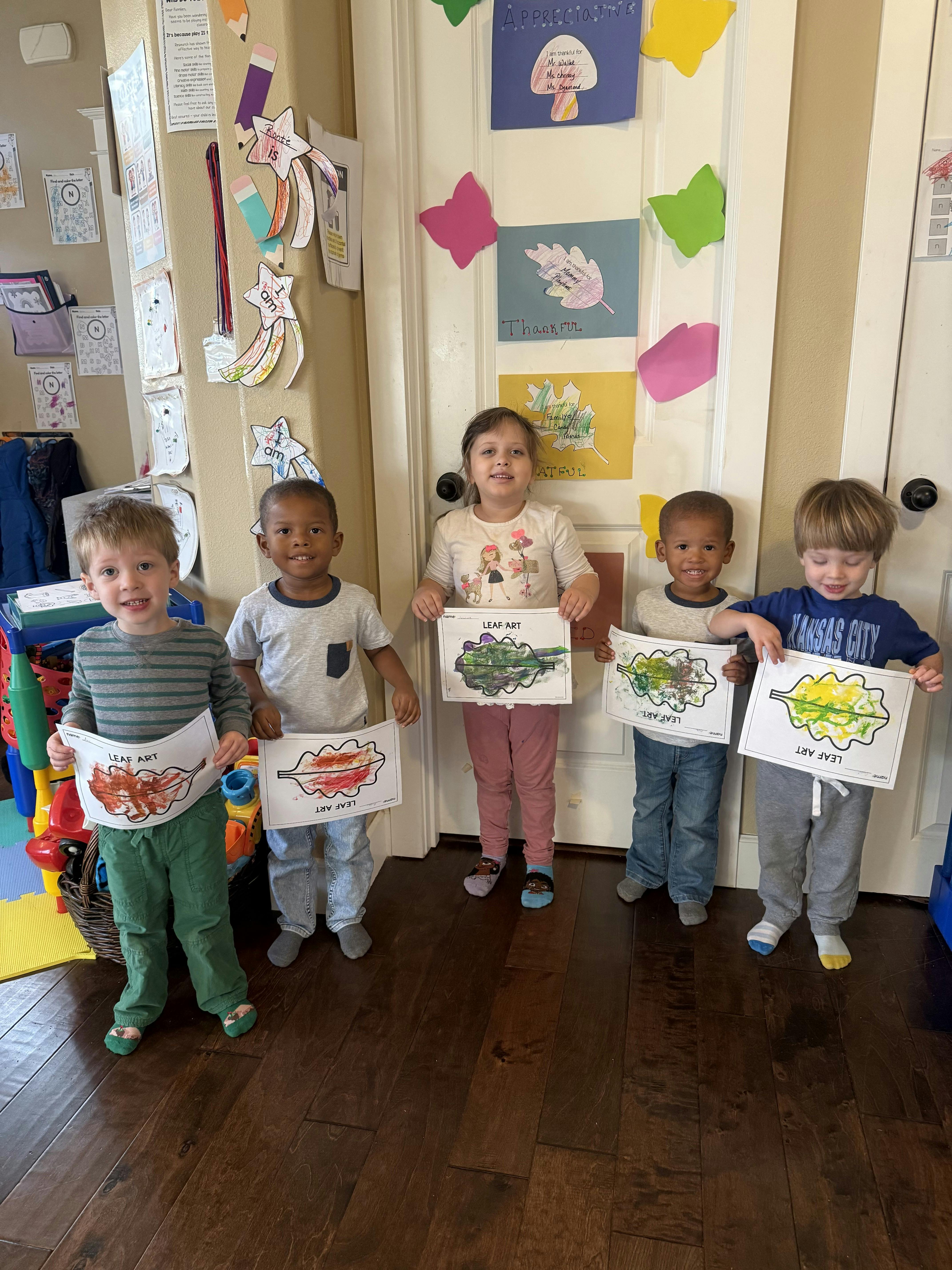 Five children holding up drawings in a classroom
