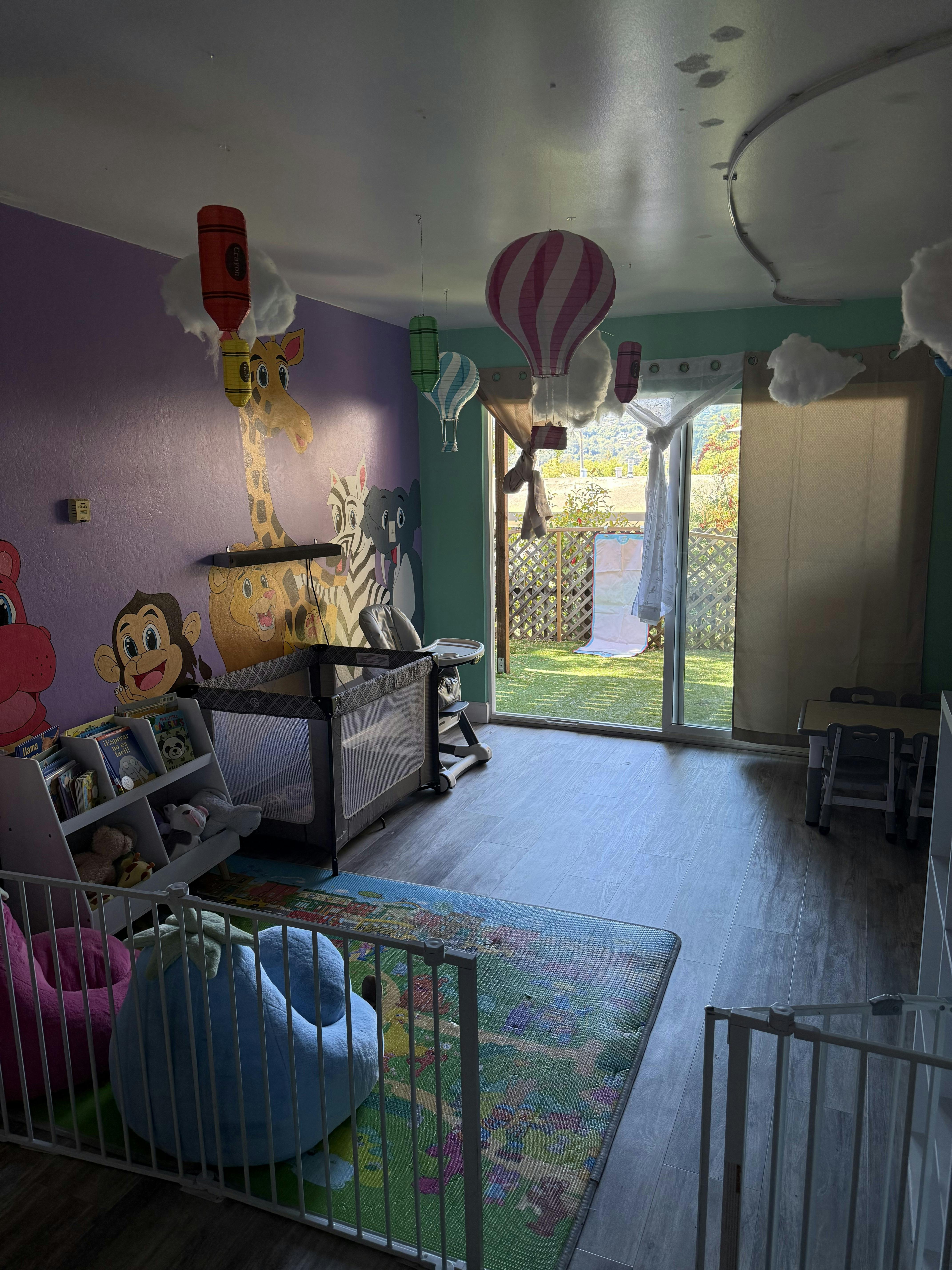 Childcare room with wall mural animal characters, playpen, and floor mat