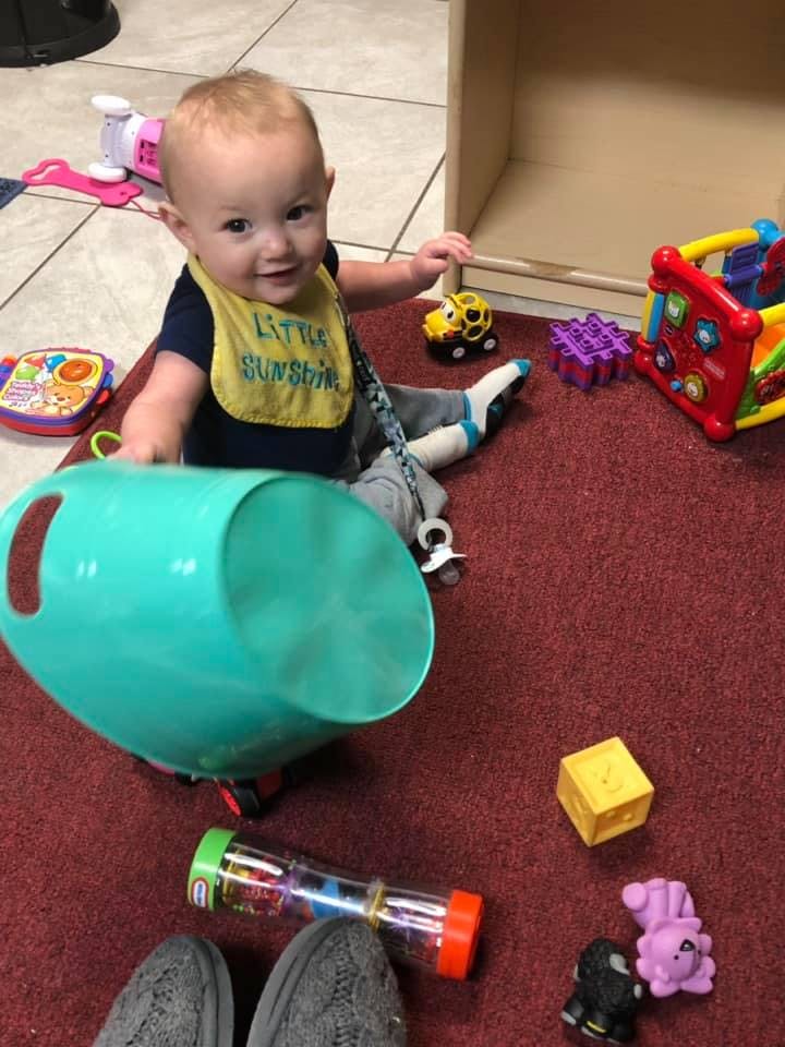 Child sitting on a rug with toys, holding a teal bucket