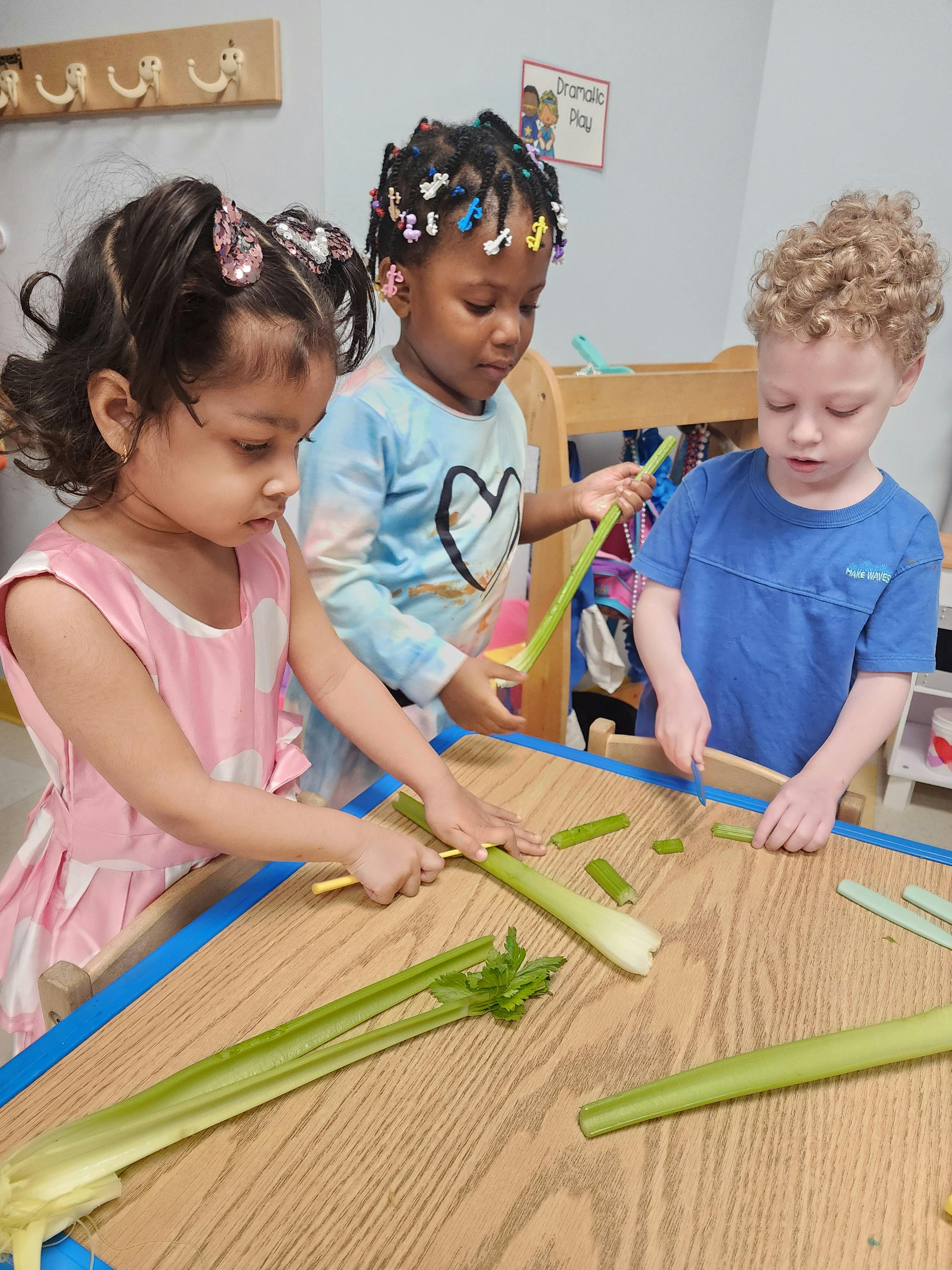Three children cutting celery stalks on a wooden table