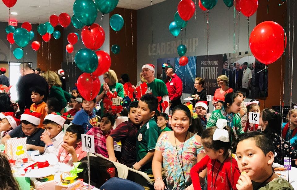Many children and adults gathered in a room with red and green balloons