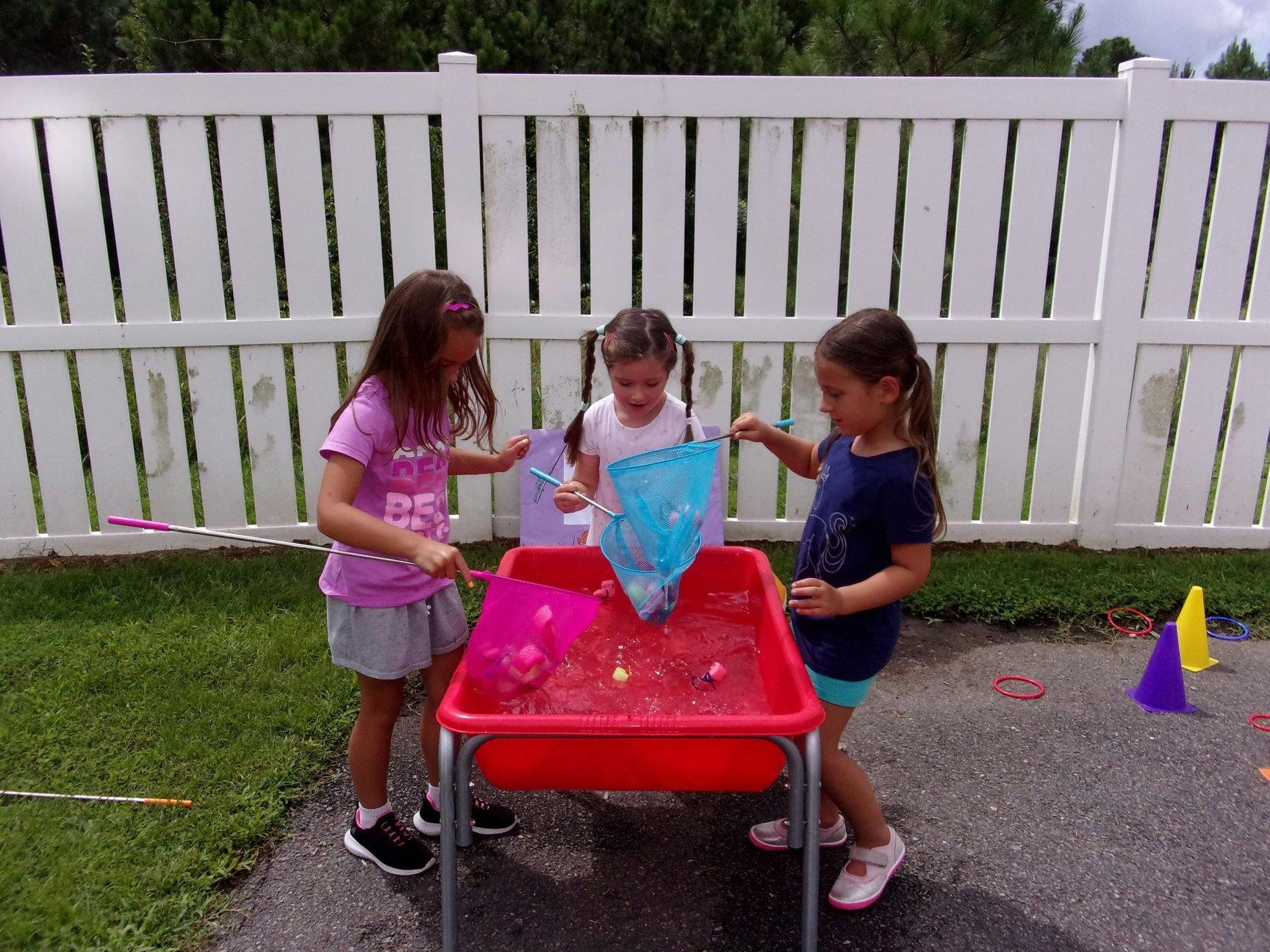 Three children playing with nets in a red water table