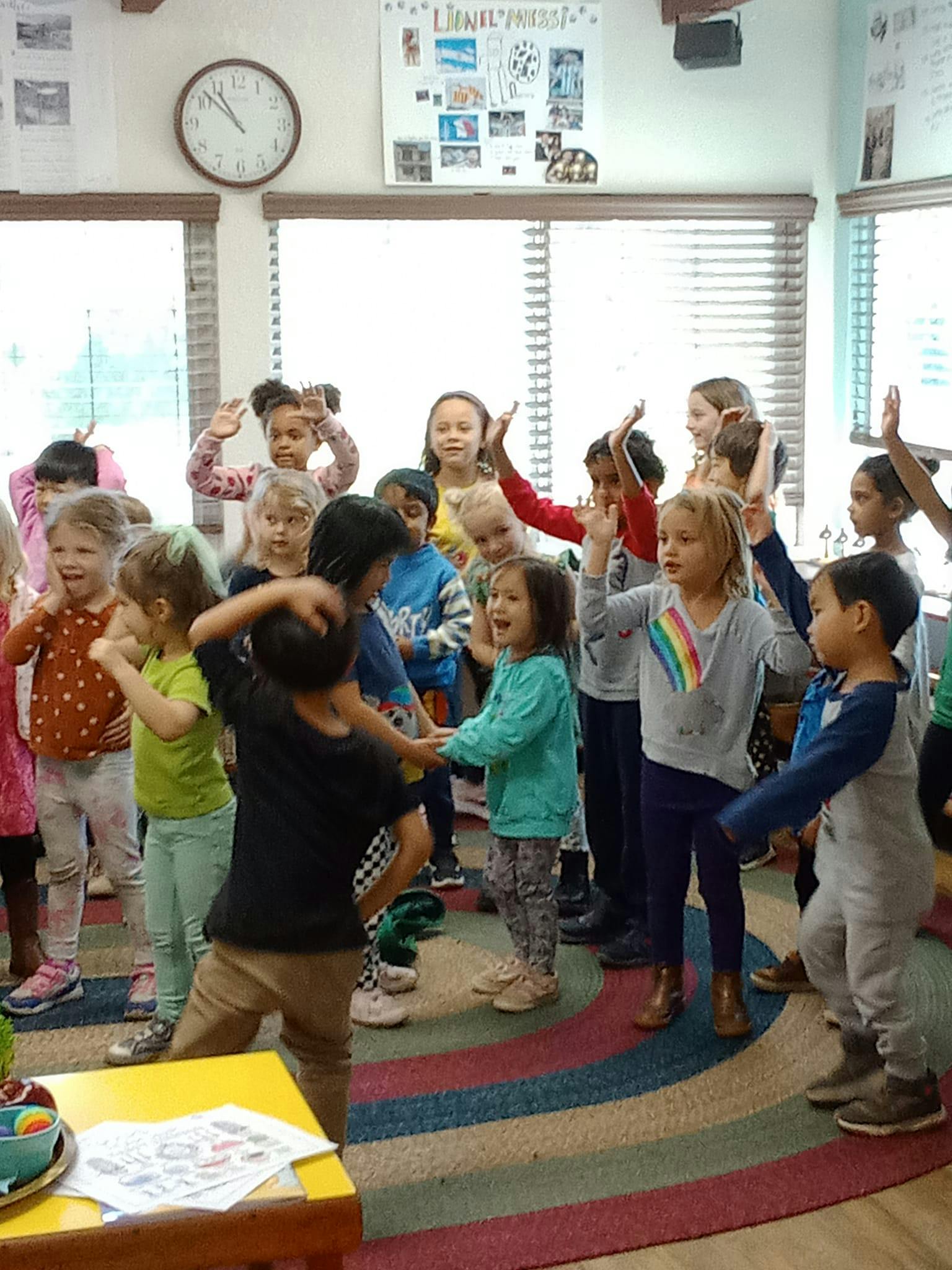 Group of children standing in a classroom, some with hands raised