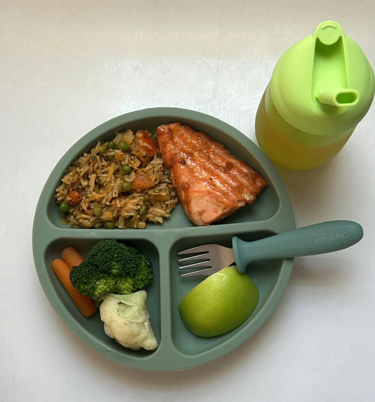 A divided plate with salmon, rice, broccoli, carrots, cauliflower, and an apple